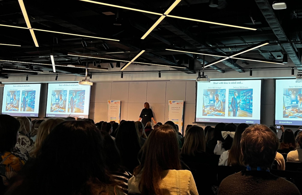 On stage at the Women in Tech SEO event in London: Joyann Boyce, the founder of Inclued AI, speaking on bias in AI. Screens show AI-generated images for the prompt to generate an image of a 'Senior SEO Director' - the AI generated images of white men. 