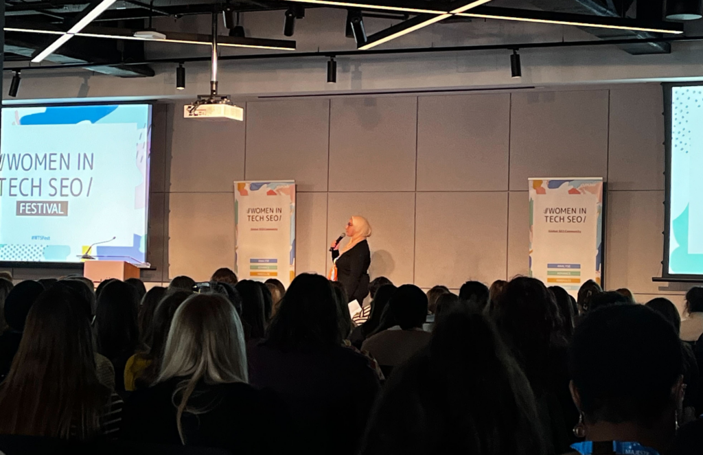 Photo of the opening remarks at the Women in Tech SEO (WTS) event in London 2024 – Founder Areej AbuAli speaking on stage.